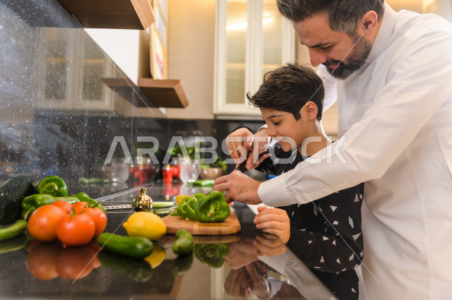 أب سعودي يشارك ابنه في اعداد وجبه الطعام في المطبخ ، مشاركة الابناء في الاعمال المنزلية ، ايماءات وجه تدل على السعادة و الفرحة