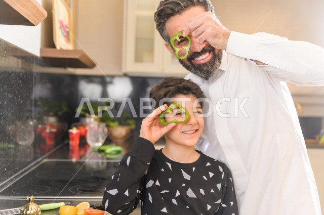 أب سعودي يشارك ابنه في اعداد وجبه الطعام في المطبخ ، مشاركة الابناء في الاعمال المنزلية ، ايماءات وجه تدل على السعادة و الفرحة