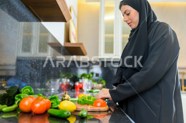 أم سعودية تقوم باعداد وجبه الطعام في المطبخ ، الاستمتاع باداء الاعمال المنزلية ، ايماءات وجه تدل على السعادة و الفرحة