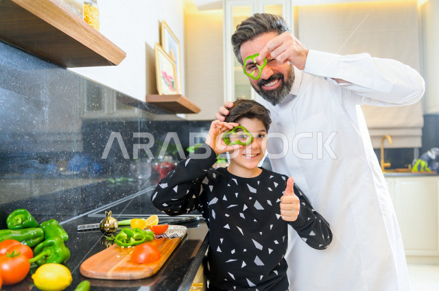 A Saudi father participates with his son in preparing the meal in the kitchen, children participating in household chores, facial gestures indicating happiness and joy