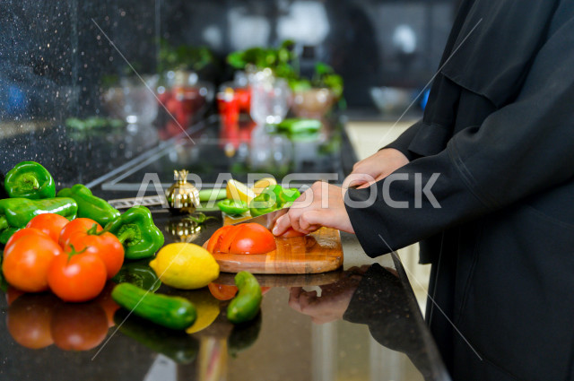 أم سعودية تقوم باعداد وجبه الطعام في المطبخ ، الاستمتاع باداء الاعمال المنزلية ، ايماءات وجه تدل على السعادة و الفرحة