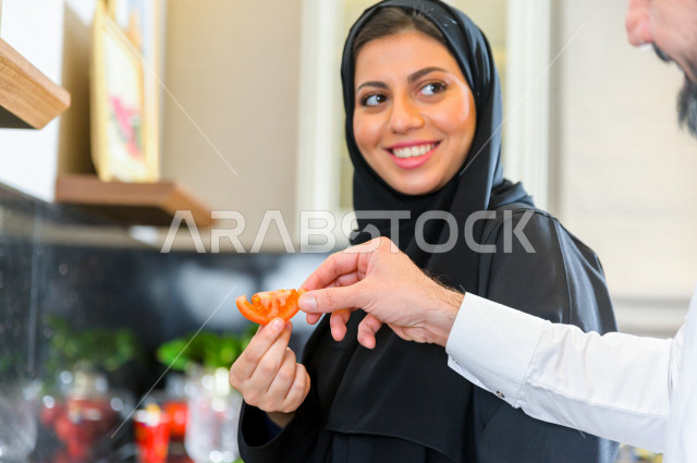 زوجان سعوديان خليجيان يتشاركان في اعداد وجبه الطعام بالمطبخ ، الاستمتاع باداء الاعمال المنزلية ، ايماءات و تعابير وجه تدل على الفرحة