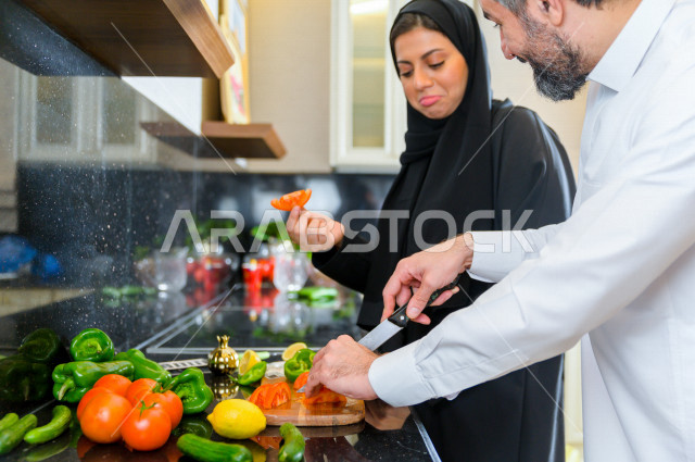 زوجان سعوديان خليجيان يتشاركان في اعداد وجبه الطعام بالمطبخ ، الاستمتاع باداء الاعمال المنزلية ، ايماءات و تعابير وجه تدل على الفرحة
