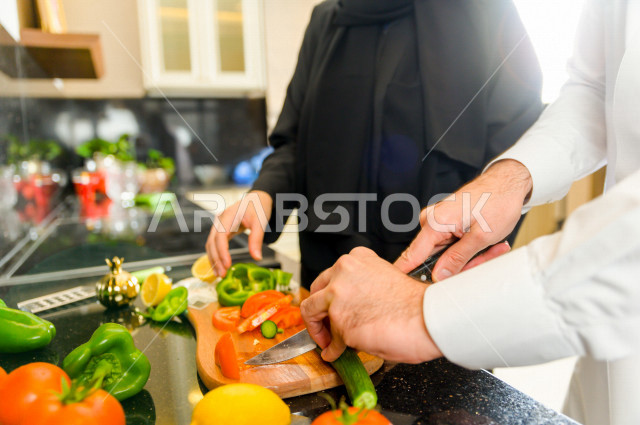 زوجان سعوديان خليجيان يتشاركان في اعداد وجبه الطعام بالمطبخ ، الاستمتاع باداء الاعمال المنزلية ، ايماءات و تعابير وجه تدل على الفرحة