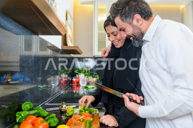 زوجان سعوديان خليجيان يتشاركان في اعداد وجبه الطعام بالمطبخ ، الاستمتاع باداء الاعمال المنزلية ، ايماءات و تعابير وجه تدل على الفرحة