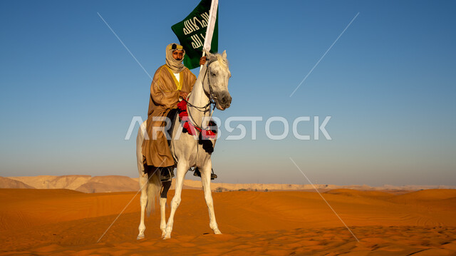 يوم بدينا  1727 م، الاحتفال مع الأحصنة بذكرى تأسيس الدولة السعودية الأولى 22 فبراير، رجل عربي خليجي سعودي يرتدي البشت والغترة مع العقال الذهبي يمتطي خيل أبيض أصيل وسط الرمال الذهبية، رفع علم وشعار التأسيس في الصحراء، مشاركة الجياد في المناسبات والأعياد الوطنية