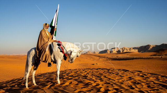الاحتفال مع الأحصنة بذكرى تأسيس الدولة السعودية الأولى 22 فبراير، رجل عربي خليجي سعودي يرتدي البشت والغترة مع العقال الذهبي يمتطي خيل أبيض أصيل وسط الرمال الذهبية، رفع علم وشعار التأسيس في الصحراء، مشاركة الجياد في المناسبات والأعياد الوطنية، يوم بدينا  1727 م