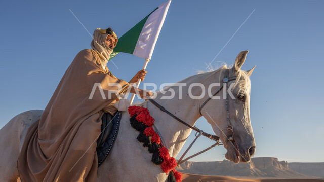 The anniversary of the founding of the first Saudi state, February 22. A Saudi Gulf Arab man wearing a bisht and a ghutra with a golden headband rides a purebred white horse in the middle of the golden sands, raising the flag and slogan of the founding in the desert, horses participating in national events and holidays, celebrating with horses the Day of Dina 1727 AD.