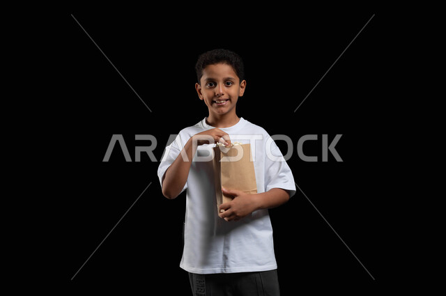 الهروب من الروتين اليومي والقيام بأنشطة ترفيهية مسلية، الاستمتاع بمشاهدة الأفلام المفضلة،  تناول الفوشار اللذيذ والمقرمش، بورتريه لفتى عربي خليجي سعودي مبتسم يرتدي الزي الكاجوال يمسك بيده كيس من الفوشار، خلفية سوداء