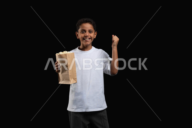 ايماءات التفاعل مع أحداث الفلم الشيقة، الاستمتاع بمواهب الفنانين والممثلين، بورتريه لفتى عربي خليجي سعودي مبتسم يرتدي الزي الكاجوال يرفع قبضته للأعلى بتعابير النصر والحماس، اضافة المتعة الى التجربة السينمائية خلال تناول الفوشار، خلفية سوداء