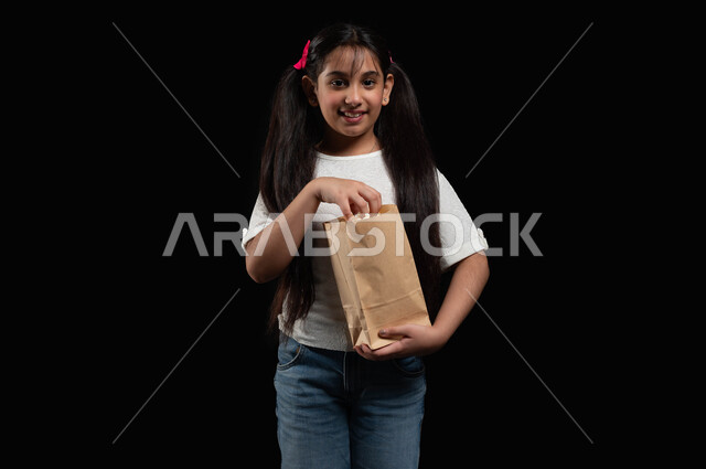 كسر الروتين والذهاب الى السينما في عطلة نهاية الأسبوع، ايماءات الفرح والسعادة، مشاهدة المسلسلات والبرامج التلفزيونية، تناول السناكات والوجبات الخفيفة، بورتريه لفتاة عربية خليجية سعودية تحمل كيس من الفشار، متعة حضور الأفلام المفضلة، خلفية سوداء