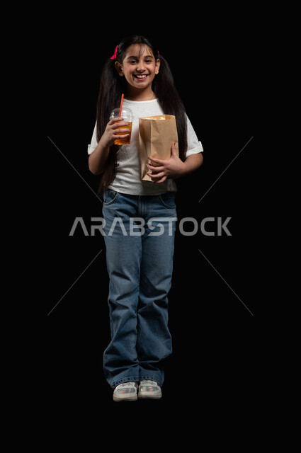 متابعة المسلسلات والبرامج التلفزيونية، ايماءات البهجة والسرور، تناول العصائر الباردة والسناكات الخفيفة، بورتريه لفتاة عربية خليجية سعودية تحمل كأس العصير والفشار، الذهاب للسينما في عطلة نهاية الأسبوع، متعة حضور الأفلام المفضلة، الطول الكامل للجسم، خلفية سوداء