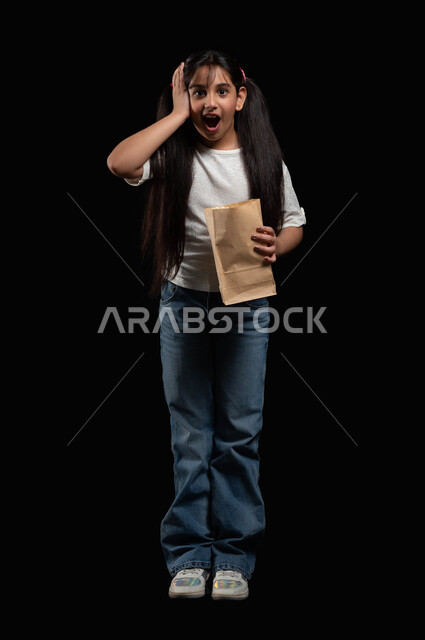 القيام بالأنشطة الترفيهية واستغلال أوقات الفراغ، الاستمتاع بحضور الأفلام المفضلة، متابعة المسلسلات والبرامج التلفزيونية، بورتريه لفتاة عربية خليجية سعودية تحمل بيديها الفوشار، ايماءات المفاجئة والدهشة، الطول الكامل للجسم، خلفية سوداء