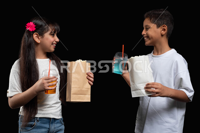 تبادل الأحاديث والتقاشات حول أحداث الفيلم، استغلال عطلة نهاية الأسبوع للذهاب الى السينما، بورتريه لولد وبنت عربيان خليجيان سعوديان يستمتعان بمشاهدة الأفلام ويحملان العصير والفشار، قضاء أوقات ممتعة ومسلية مع الأخوة، ايماءات السعادة والسرور، خلفية سوداء