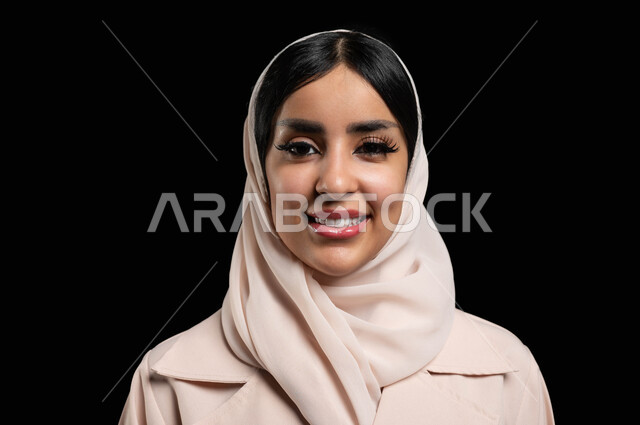 The concept of elegance and attention to external appearance, a close-up portrait of a veiled Saudi Arabian Gulf woman wearing a sugar-colored abaya, smiling and standing upright, looking at the camera with gestures of happiness and pleasure, taking personal photos for official documents, black background