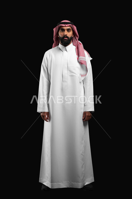 التقاط صور شخصية للوثائق الرسمية، الاهتمام بالأناقة والمظهر الخارجي، الوقوف باستقامة بتعابير الجدية والحزم، بورتريه لرجل عربي خليجي سعودي يرتدي الشماغ والثوب السعودي التقليدي ينظر الى الكاميرا بايماءات الرجولة والثقة بالنفس، صورة الجسم بالكامل، خلفية سوداء