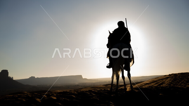 The founding of the first Saudi state, February 22, a silhouette of a Saudi Arabian Gulf horseman practicing the hobby of horse riding in one of the Kingdom’s deserts at sunset, the love of raising horses passed down among the people of the country, riding on the back of a purebred white horse over the sand dunes, a memory of the Day of Dina 1727 AD, Salwit