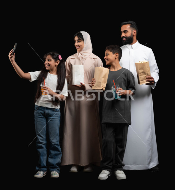 Using a mobile phone to take a selfie, preserving special moments, a happy family atmosphere, a portrait of a Saudi Gulf Arab family, watching movies and series, entertaining weekend activities, enjoying popcorn and cold drinks, a black background