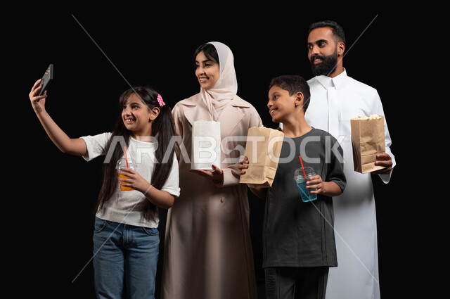 الاحتفاظ باللحظات المميزة، استخدام الموبايل لالتقاط صورة سيلفي، أجواء عائلية سعيدة، بورتريه لأسرة عربية خليجية سعودية، مشاهدة الافلام والمسلسلات، أنشطة عطلة نهاية الاسبوع الترفيهية، الاستمتاع بتناول الفوشار والمشروبات الباردة، خلفية سوداء