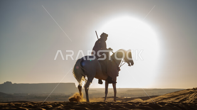 The founding of the first Saudi state, February 22, a silhouette of a Saudi Arabian Gulf horseman practicing the hobby of horse riding in one of the Kingdom’s deserts at sunset, the love of raising horses passed down among the people of the country, riding on the back of a purebred white horse over the sand dunes, a memory of the Day of Dina 1727 AD, Salwit
