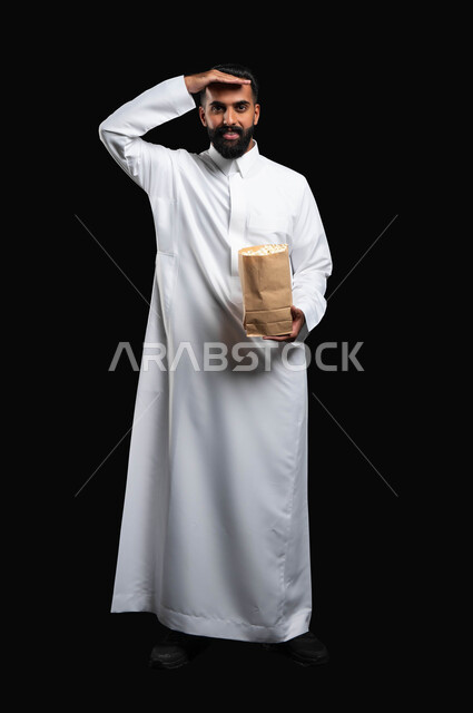 الوقوف باستقامة والنظر إلى الكاميرا بايماءات البحث و الترقب، الاستمتاع بمشاهدة الأفلام والمسلسلات، بورتريه لرجل عربي خليجي سعودي يرتدي الثوب التقليدي الأبيض يحمل بيده كيس من الفوشار يضع يده على جبينه، تناول الوجبات الخفيفة والسناك، متابعة برامج التلفاز، خلفية سوداء