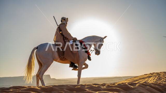 توارث حب وشغف تربية الخيول بين أبناء الوطن، التجول على ظهر الفرس الأبيض الأصيل في إحدى صحاري المملكة, يوم بدينا 1727 م, ذكرى تأسيس الدولة السعودية الأولى 22 فبراير, فارس عربي خليجي سعودي يرتدي البشت والغترة مع العقال الذهبي يمارس هواية ركوب الخيل في النهار