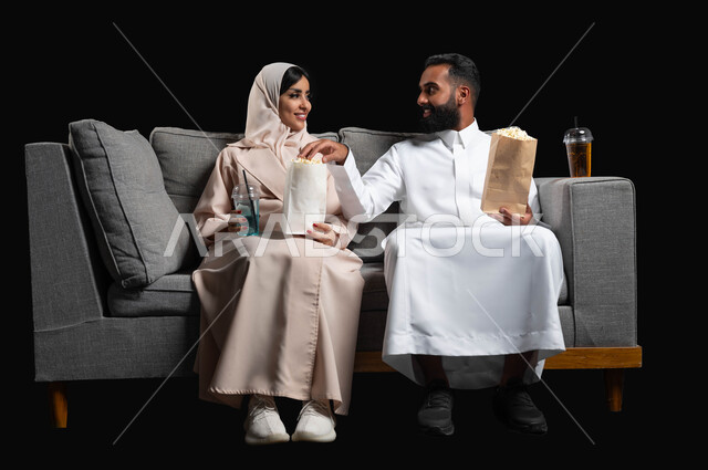 تبادل نظرات الحب والمودة، متابعة المسلسلات والبرامج التفزيونية، الاستمتاع بقضاء أوقات رومانسية، تناول الفوشار والمشروبات الباردة، بورتريه لزوجين عربيين خليجيين سعوديين يجلسان على كنبه مريحة يقومان بمشاهدة الافلام، أنشطة عطلة نهاية الأسبوع، خلفية سوداء