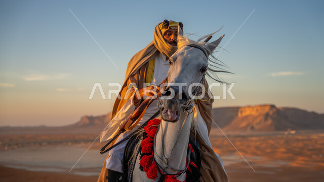 ممارسة هواية ركوب الخيل في إحدى صحاري المملكة، ذكرى يوم بدينا 1727 م، تأسيس الدولة السعودية الأولى 22 فبراير, فارس عربي خليجي سعودي يرتدي البشت والغترة مع العقال يتجول على ظهر فرسه الأبيض الأصيل فوق الرمال الذهبية، توارث حب وشغف تربية الخيول بين أبناء الوطن