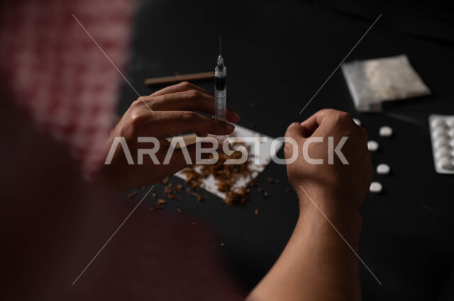 العادات السلوكية الضارة وتعاطي المواد السامة، المعاناة من الاضطرابات النفسية والمشاكل الصحية، صورة مقربة لرجل عربي خليجي سعودي يرتدي الشماغ والثوب التقليدي يجلس على الاريكة يقوم بأخذ جرعة مخدرة، حقن المخدرات في الأوردة، الآثار السلبية للادمان والتعاطي