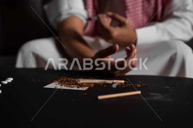 العادات السلوكية الضارة وتعاطي المواد السامة، المعاناة من الاضطرابات النفسية والمشاكل الصحية، صورة مقربة لرجل عربي خليجي سعودي يرتدي الشماغ والثوب التقليدي يجلس على الاريكة يقوم بأخذ جرعة مخدرة، حقن المخدرات في الأوردة، الآثار السلبية للادمان والتعاطي