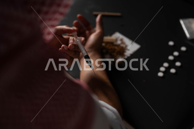 المعاناة من الاضطرابات النفسية والمشاكل الصحية، تعاطي المخدرات عن طريق الحقن في الأوردة، الآثار السلبية للادمان، القيام بعادات سلوكية ضارة وتعاطي المواد السامة، صورة مقربة لرجل عربي خليجي سعودي يرتدي الشماغ والثوب التقليدي يقوم بأخذ جرعة مخدرة
