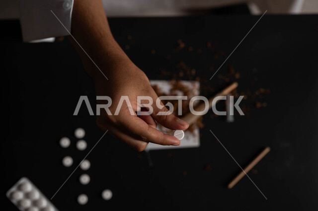 القيام بعادات سلوكية ضارة وتعاطي المواد السامة، المعاناة من الاضطرابات النفسية والمشاكل الصحية، صورة مقربة ليد رجل عربي خليجي سعودي يمسك الحبوب المخدرة، الآثار السلبية للادمان والتعاطي