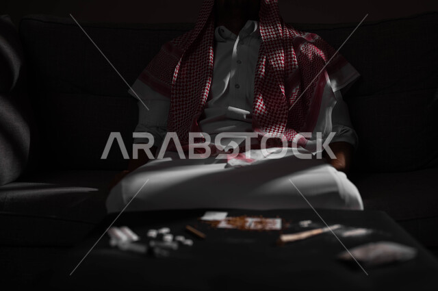 Punishing oneself and remorse of conscience, suffering from psychological disorders and health problems, a portrait of a Saudi Gulf Arab man wearing a shemagh and traditional dress sitting on the sofa with an expression of fatigue and remorse, the negative effects of addiction and abuse, engaging in harmful behavioral habits and taking toxic substances.