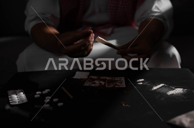 المعاناة من الاضطرابات النفسية والمشاكل الصحية، صورة مقربة لرجل عربي خليجي سعودي يرتدي الشماغ والثوب التقليدي يجلس على اريكة يقوم بلف عقب السجائر، الأثار السلبية للادمان على التبغ والمخدرات، القيام بعادات سلوكية ضارة وتعاطي المواد السامة