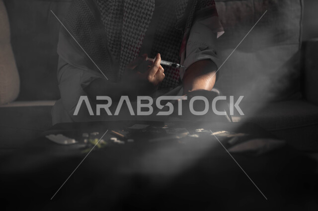 Injecting drugs into veins, the negative effects of addiction, engaging in harmful behavioral habits and taking toxic substances, suffering from psychological disorders and health problems, a close-up silhouette of a Saudi Gulf Arab man wearing a shemagh and traditional dress, sitting on the sofa taking an anesthetic needle.