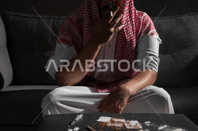 الادمان على التبغ والسجائر، تعاطي مواد ضارة وسامة، عادات سلوكية خاطئة، الإصابه بأمراض الجهاز التنفسي، صورة مقربة لشاب عربي سعودي خليجي يرتدي الشماغ والثوب التقليدي يقوم  بسحب نفس عميق من السيجارة