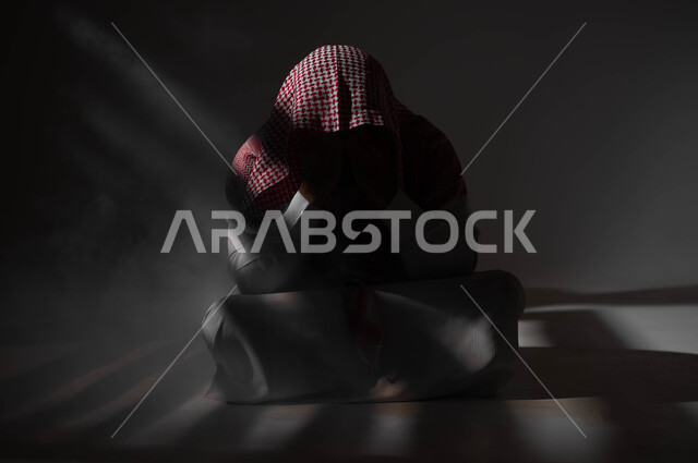 Punishing oneself and remorse, suffering from psychological disorders and health problems, a portrait of a Saudi Gulf Arab man wearing a shemagh and traditional dress, sitting on the ground with an expression of fatigue and remorse, the negative effects of addiction and abuse, a black background.