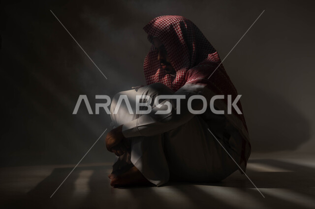 الإنعزال النفسي والشخصية الانطوائية، المعاناة من الاضطرابات النفسية، بورتريه لرجل عربي خليجي سعودي يرتدي الزي التقليدي يجلس على الارض مصاب بالإكتئاب والإنهيار العصبي، الآثار السلبية للادمان والتعاطي، معاقبة النفس وتأنيب الضمير، خلفية سوداء