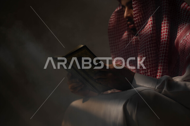 تلاوة وقراءة القرآن الكريم، التوبة والرجوع الى الله تعالى، بورتريه مقرب لرجل عربي سعودي خليجي يرتدي الشماغ والثوب التقليدي يحمل بيده المصحف الشريف, الشعور بالخشوع والطمأنينه, الإكثار من الذكر والإجتهاد في العباده في شهر رمضان, خلفية سوداء