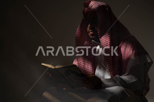 التوبة والرجوع الى الله تعالى، تلاوة وقراءة القرآن الكريم، بورتريه مقرب لرجل عربي سعودي خليجي يرتدي الشماغ والثوب التقليدي يحمل بيده المصحف الشريف, الشعور بالخشوع والطمأنينه, الإكثار من الذكر والإجتهاد في العباده في شهر رمضان, خلفية سوداء