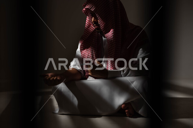 الآثار السلبية للادمان والتعاطي، القيام بعادات سلوكية ضارة وتعاطي المواد السامة، المعاناة من الاضطرابات النفسية والمشاكل الصحية، بورتريه لرجل عربي خليجي سعودي يرتدي الشماغ والثوب التقليدي يجلس على الارض يقوم بأخذ جرعة مخدرة، حقن المخدرات في الأوردة، خلفية سوداء