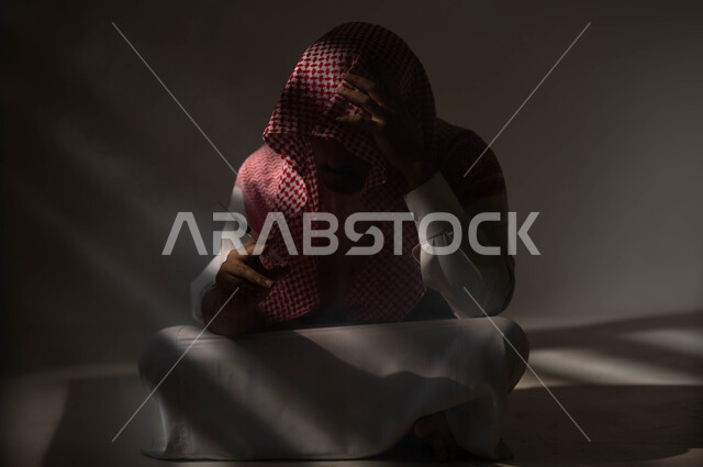 الآثار السلبية للادمان والتعاطي، القيام بعادات سلوكية ضارة وتعاطي المواد السامة، المعاناة من الاضطرابات النفسية والمشاكل الصحية، بورتريه لرجل عربي خليجي سعودي يرتدي الشماغ والثوب التقليدي يجلس على الارض يقوم بأخذ جرعة مخدرة، حقن المخدرات في الأوردة، خلفية سوداء