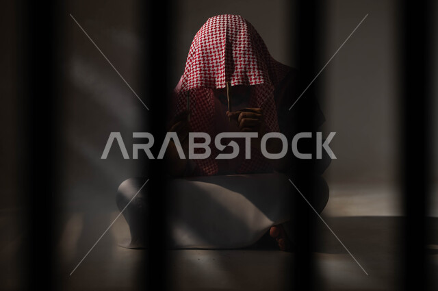 المعاناة من الاضطرابات النفسية والمشاكل الصحية، الادمان على التبغ والمخدرات، بورتريه لرجل عربي خليجي سعودي يرتدي الشماغ والثوب التقليدي يجلس على الأرض يمسك بيديه عقب سيجارة، عادات سلوكية ضارة وتعاطي مواد سامة، معاقبة النفس وتأنيب الضمير، خلفية سوداء