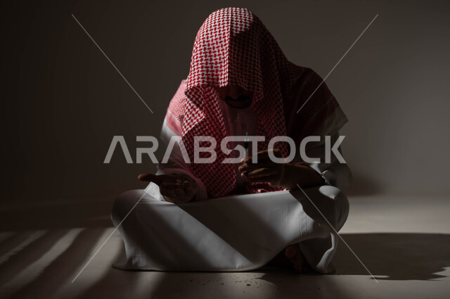 القيام بعادات سلوكية ضارة وتعاطي المواد السامة، المعاناة من الاضطرابات النفسية والمشاكل الصحية، بورتريه لرجل عربي خليجي سعودي يرتدي الشماغ والثوب التقليدي يجلس على الارض يقوم بأخذ جرعة مخدرة، الآثار السلبية للادمان والتعاطي، حقن المخدرات في الأوردة، خلفية سوداء