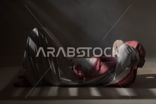 إيجاد حل لمشكلة ما، التأمل والتخطيط للمستقبل، الشعور بالملل والتعب من ضغوطات الحياة والعمل، بورتريه من الجانب لرجل عربي خليجي سعودي يرتدي الثوب والشماغ التقليدي يستلقي على الأرض ويضع يديه خلف رأسه بإيماءات التفكير، التمعن والتركيز وشرود الذهن، خلفية سوداء