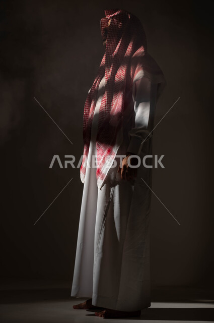 الشعور بالملل والتعب من ضغوطات الحياة والعمل، التأمل والتخطيط للمستقبل، إيجاد حل لمشكلة ما، بورتريه من الجانب لرجل عربي خليجي سعودي يرتدي الثوب والشماغ التقليدي ينظر إلى شيء ما بإيماءات التفكير، التمعن والتركيز وشرود الذهن، صورة الجسم بالكامل، خلفية سوداء
