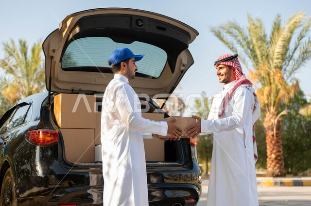 طلب المشتريات أونلاين، عملية نقل الطلبات للزبائن، استلام الطلبية من سيارة البضائع، رجل عربي خليجي سعودي يرتدي الثوب التقليدي والشماغ يقوم بأخذ صندوق المشتريات، خدمة الشحن السريعة والموثوقة، التسوق الذكي الآمن