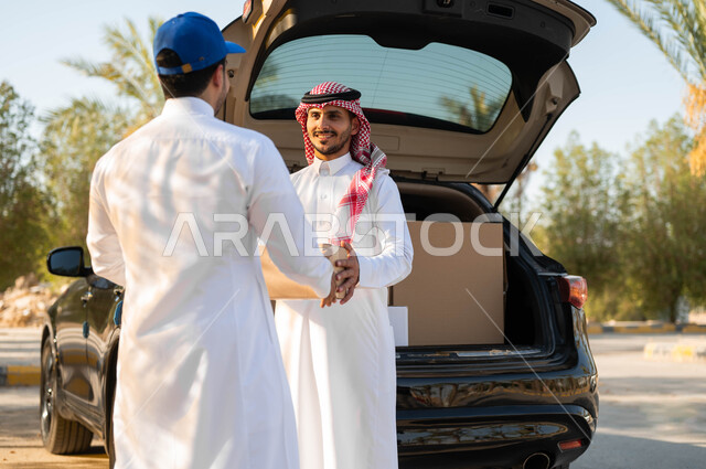 Fast and reliable shipping service, safe smart shopping, the process of transferring orders to customers, receiving the order from the goods vehicle, a Saudi Gulf Arab man wearing the traditional thobe and shemagh taking the shopping box, ordering purchases online.