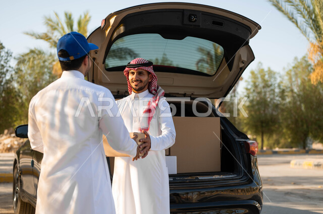 التسوق الذكي الآمن، عملية نقل الطلبات للزبائن، استلام الطلبية من سيارة البضائع، رجل عربي خليجي سعودي يرتدي الثوب التقليدي والشماغ يقوم بأخذ صندوق المشتريات، خدمة الشحن السريعة والموثوقة، طلب المشتريات أونلاين