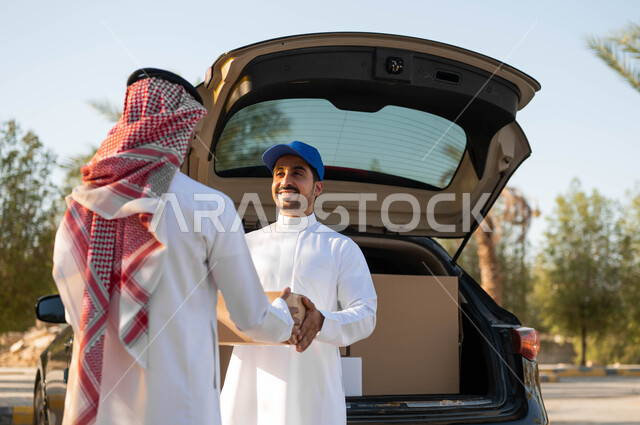 كراتين الشحن والتوصيل الأونلاين، رجل عربي خليجي سعودي يرتدي الثوب التقليدي والشماغ  يقوم باستلام الطرد من المندوب، ايماءات الرضا والسعادة لوصول الطلبية بشكل سريع